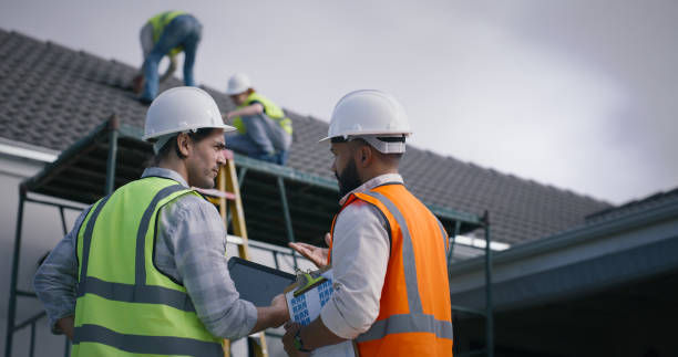 Roof inspection in Staten Island, NY — two men in hard hats and vests standing on a roof discussing construction plans.