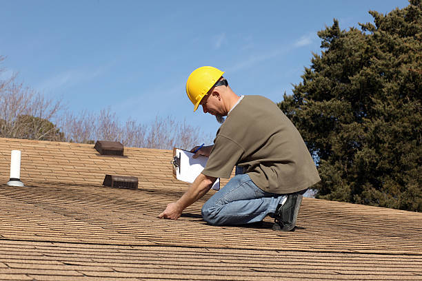 A man in a hard hat and yellow safety vest conducts a roof inspection, focusing on the structure's condition.