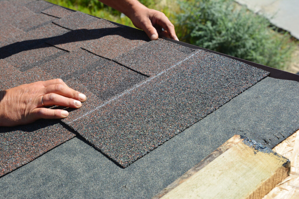 A person installing asphalt shingles on a roof, carefully placing each shingle in position for proper coverage.