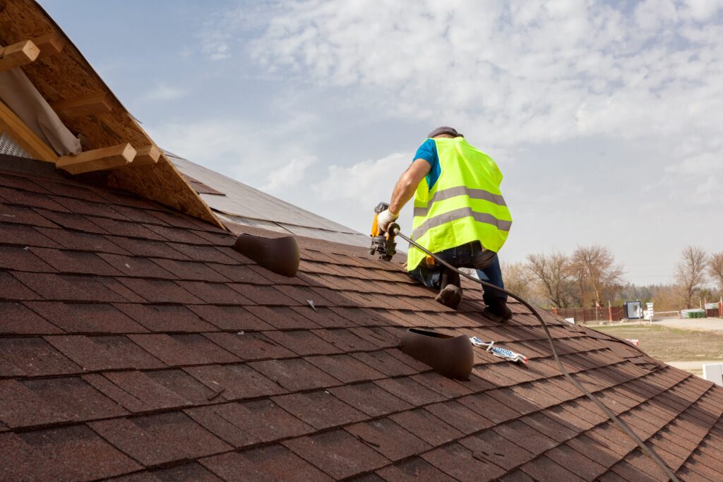 A man in a yellow vest is working on a roof, engaged in roofing tasks with tools and materials around him.