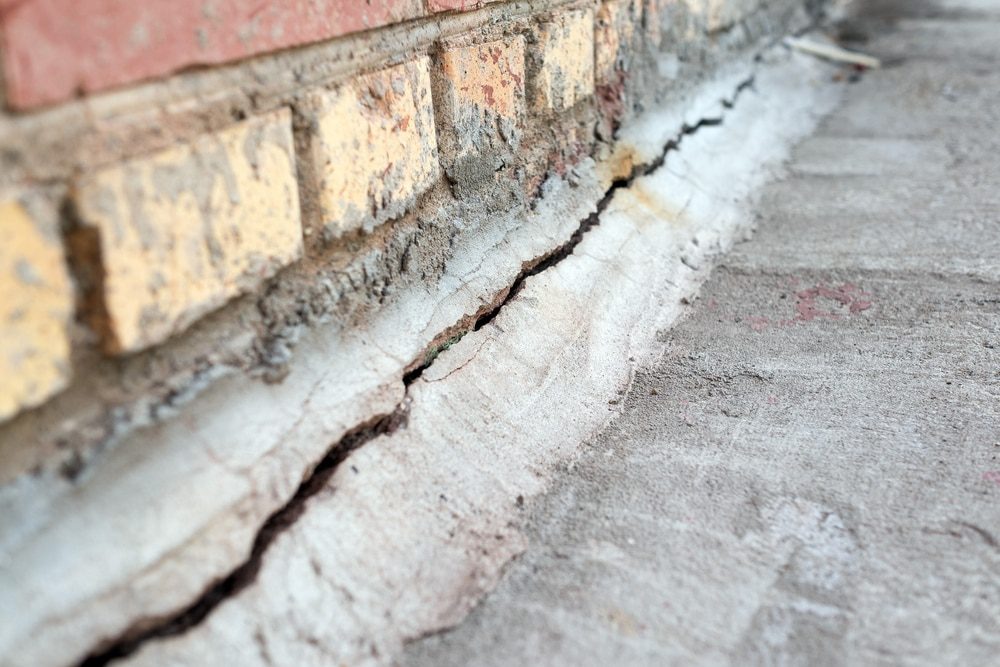 A crack in the sidewalk adjacent to a brick wall, indicating a potential masonry problem.