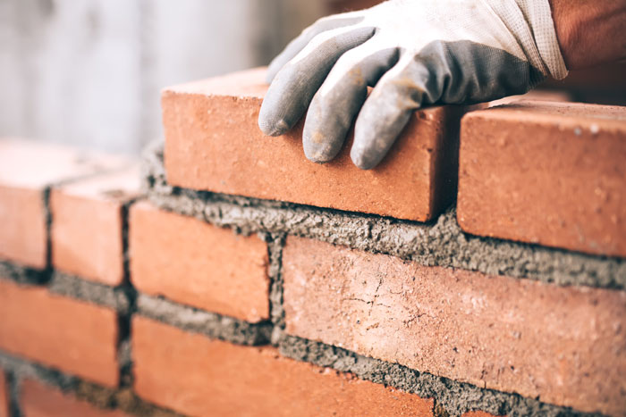 A person wearing gloves is carefully placing bricks on a wall during a masonry restoration project.