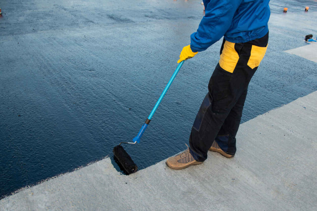 The Impact of Waterproofing on Roofing: Bronx, NY Homeowners’ Guide 2 A man brushes concrete to clean it, preparing the surface for waterproofing treatment.