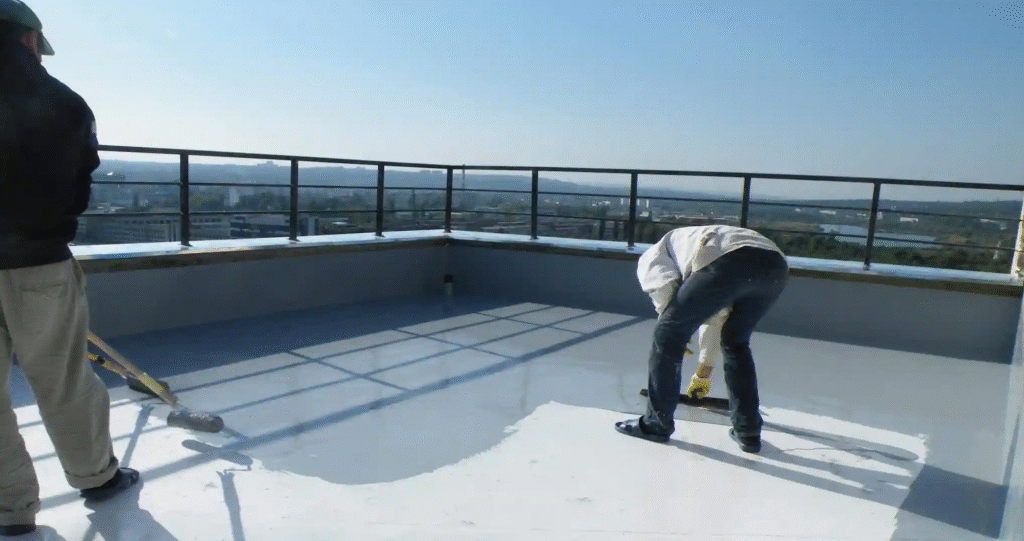 Two men applying waterproof white paint to a roof surface for protection against water damage.