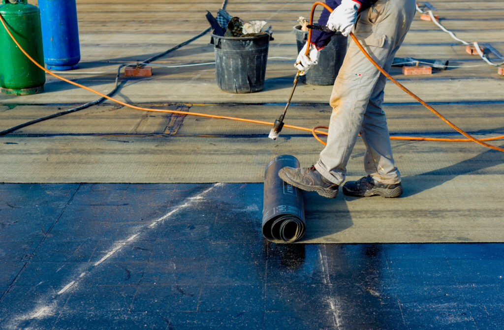 The Impact of Waterproofing on Roofing: Bronx, NY Homeowners’ Guide 1 A man applies waterproofing on a roof using a hose to ensure protection against water damage.