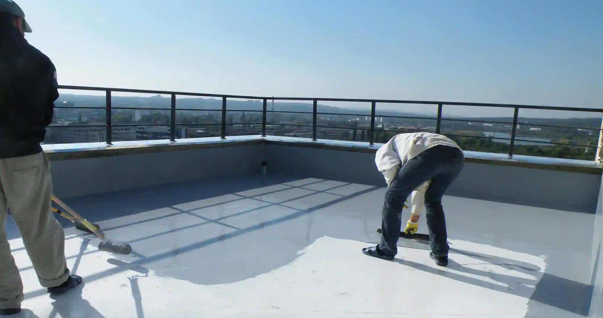 Two men applying waterproof white paint to a roof surface for protection against water damage.