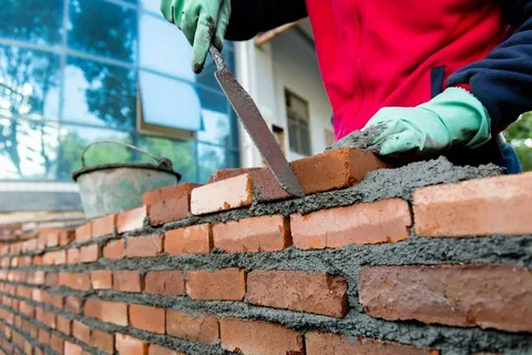 What Are the Essential Services Provided by Masonry Contractors? 2 Professional masonry contractors laying cement mortar on a red brick wall construction site