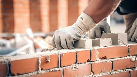 What Are the Essential Services Provided by Masonry Contractors? 1 Bricklayer from a team of masonry contractors using a trowel to apply mortar