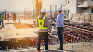 Two construction engineers in hard hats and safety vests overlooking an active building site for General Contractor Services