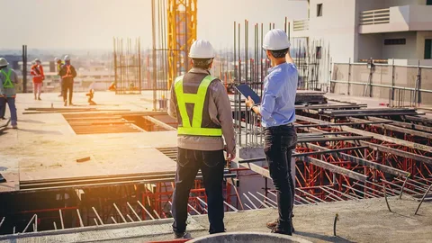 Two construction engineers in hard hats and safety vests overlooking an active building site for General Contractor Services