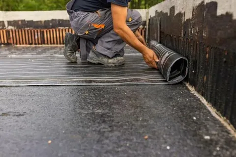 What Are the Signs Your HOA Property Needs Waterproofing? 2 Worker installing a black waterproofing membrane to protect a structural surface