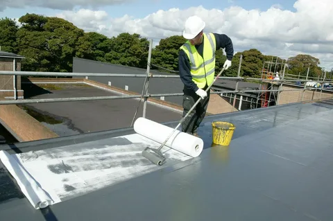 What Are the Signs Your HOA Property Needs Waterproofing? 1 Construction worker in an orange safety vest unrolling a black membrane sheet for flat roof Waterproofing